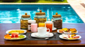 Un buffet de petit-déjeuner proposant divers plats et boissons, servi au bord de la piscine.