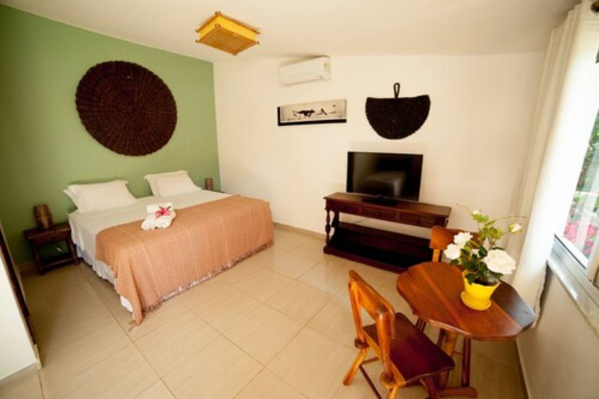 A bedroom with a bed, a TV, a dining table with chairs, and a window with a view.