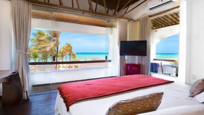 A hotel room with a large bed, a TV, and a balcony with a view of the beach and palm trees. - Vila Coqueiros (Caucaia)