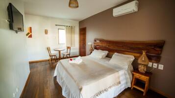 A bedroom with a large bed, a wooden headboard, a bedside table with a lamp, a TV mounted on the wall, and a small table with chairs in the corner.