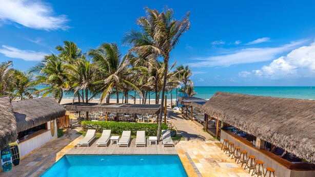 A pool area with lounge chairs, a bar, and thatched-roof structures. - Vila Coqueiros (Caucaia)