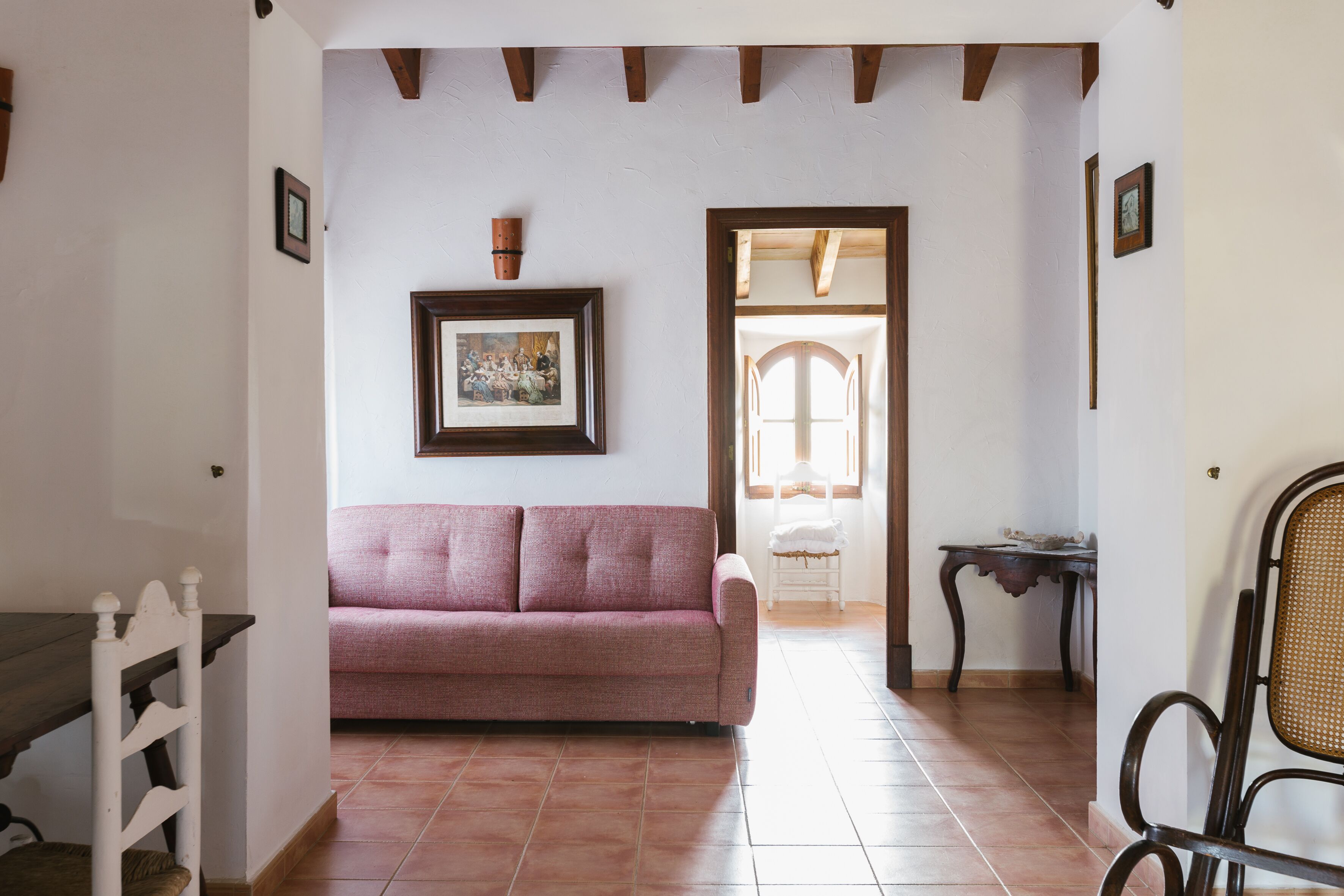 A room with a wooden ceiling, a pink sofa, a framed picture, and a chair.