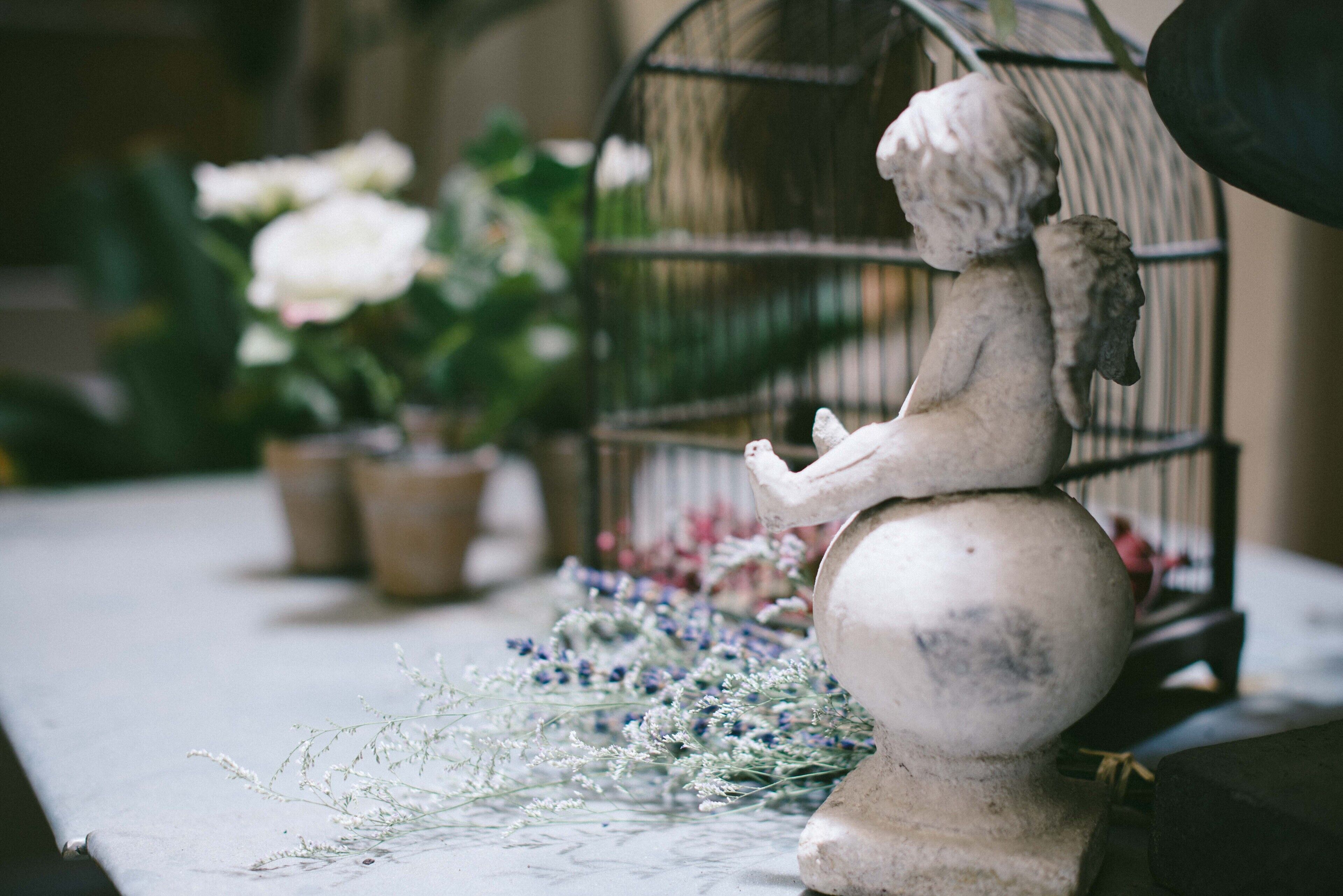 Una estatua de una figura sentada sobre una barandilla, rodeada de macetas con plantas y flores.