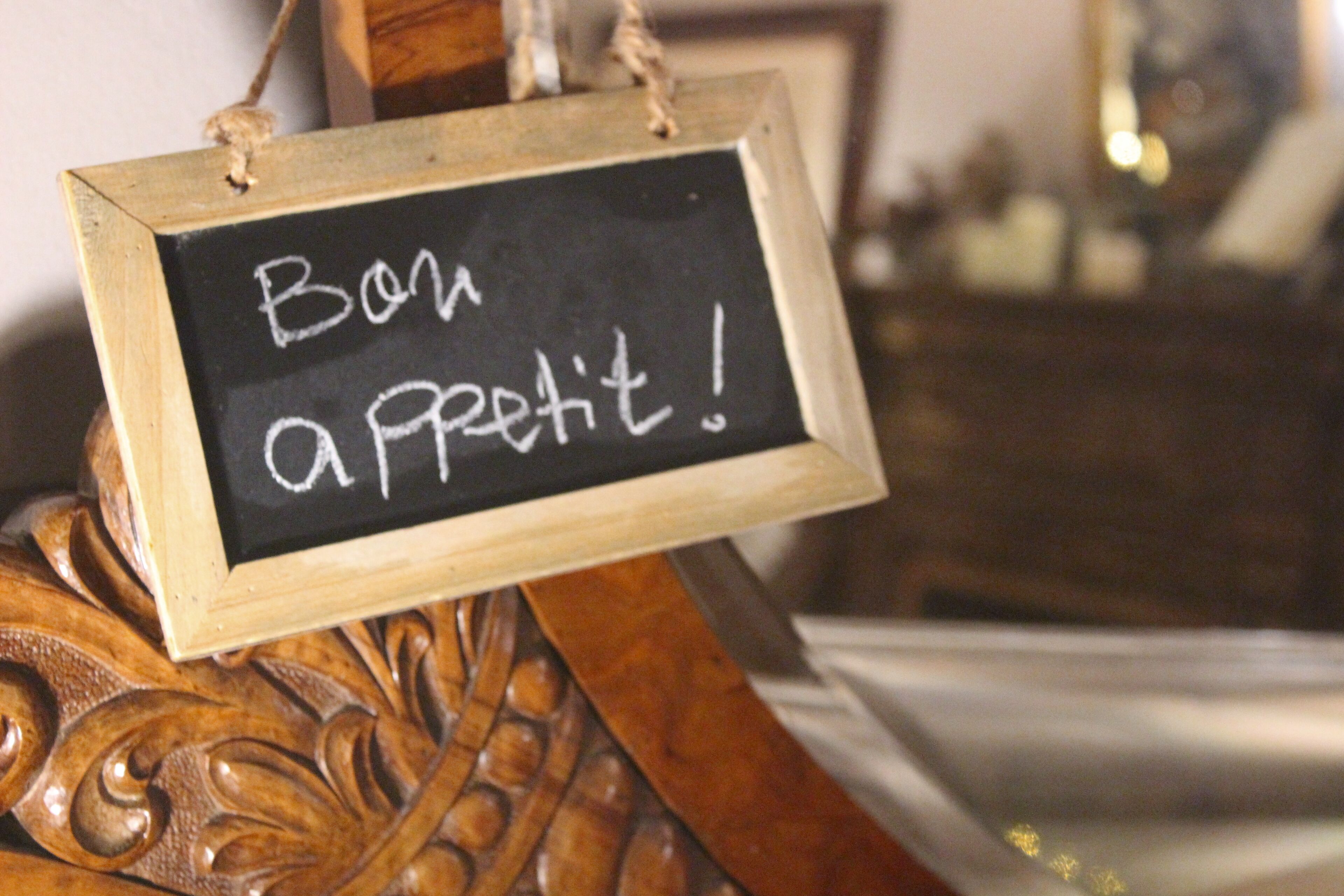 Une enseigne en bois portant l’inscription « Bon appétit ! » en craie blanche sur un tableau noir, suspendue à une structure en bois.