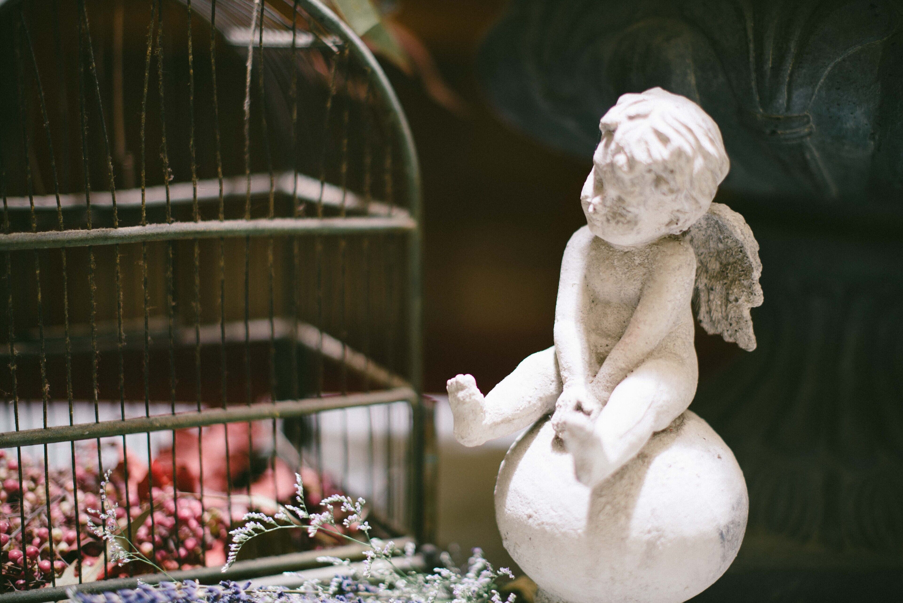 A statue of a figure sitting on a ball next to a birdcage with flowers.