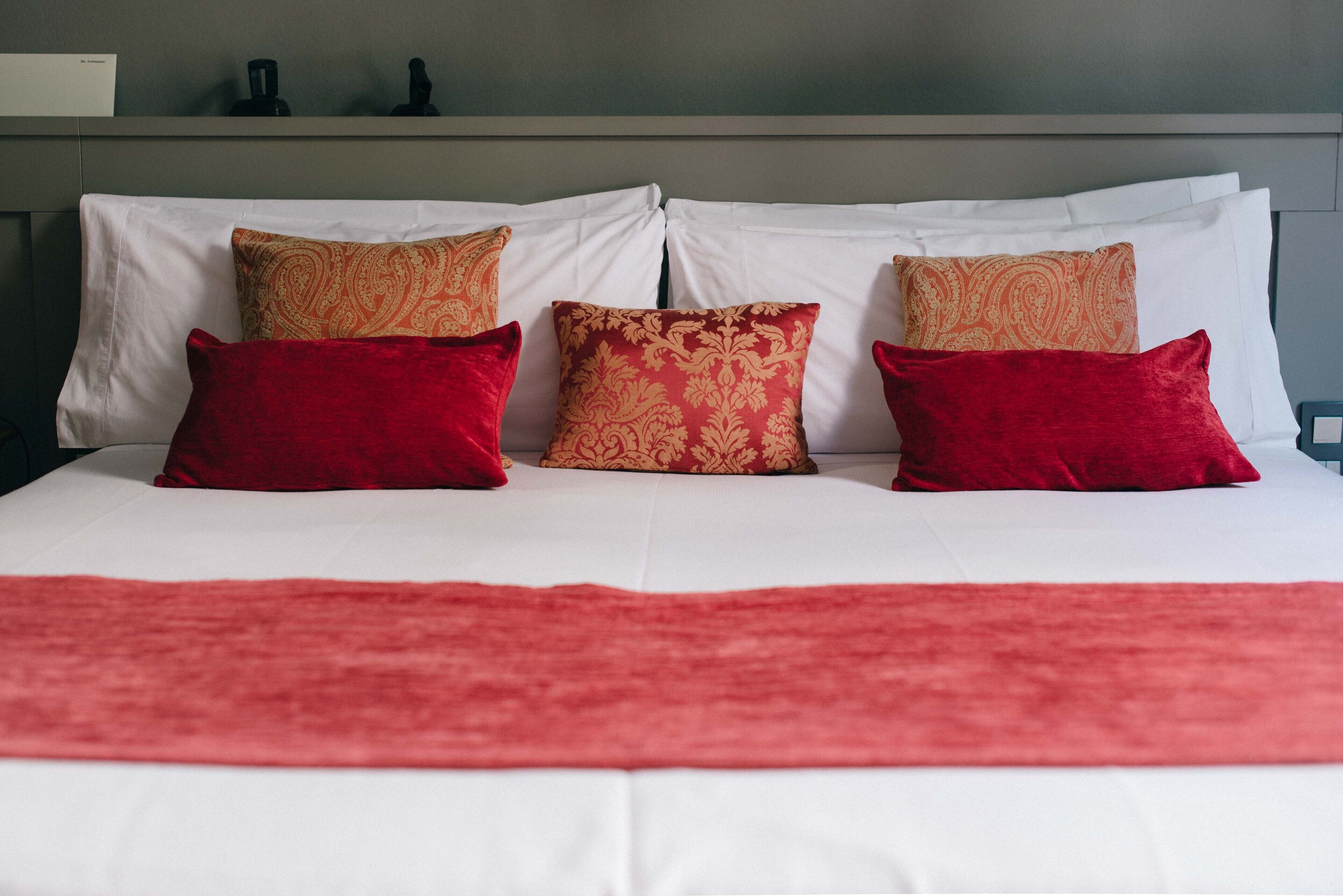 Een bed met witte lakens en kussens met een rood en gouden patroon.