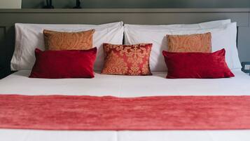 Een bed met witte lakens en kussens met een rood en gouden patroon.