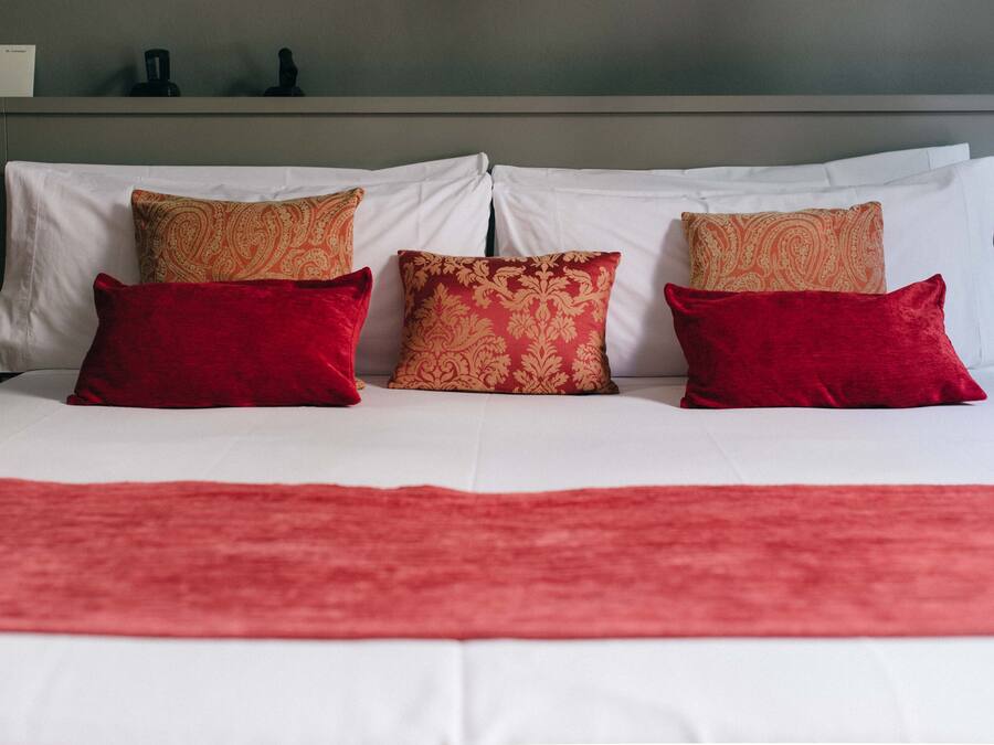 Een bed met witte lakens en kussens met een rood en gouden patroon.