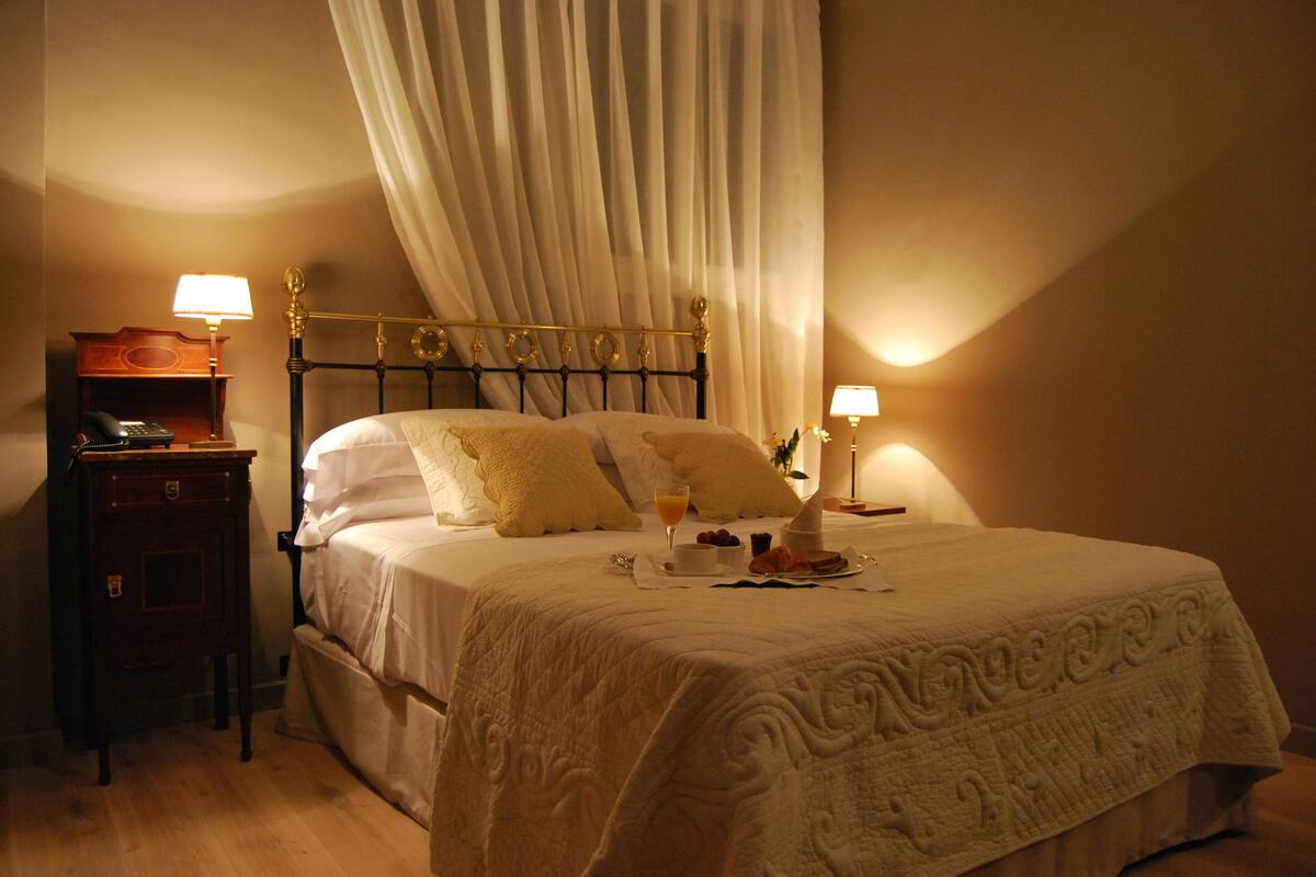 A neatly made bed with a white bedspread, two bedside lamps, and a nightstand with a lamp and a telephone.
