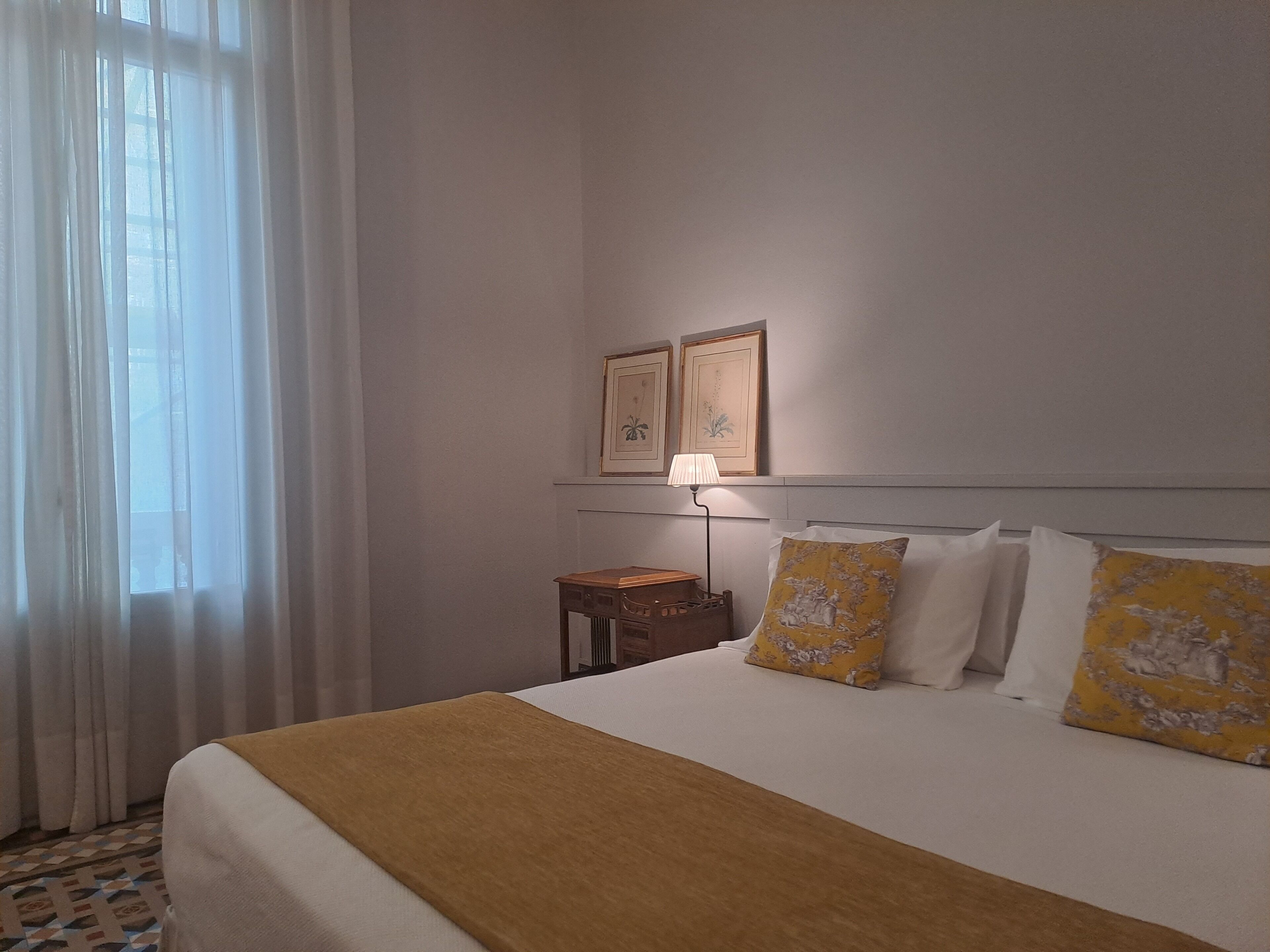Habitación de hotel con una cama grande, una mesita de noche, una lámpara y dos cuadros en la pared.