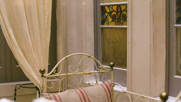 A bed with a metal frame, a striped pillow, and a window with a stained glass design.