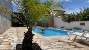 A potted palm plant in a stone planter on a patio with a pool in the background. - Pousada Mar Azul (Paraty)