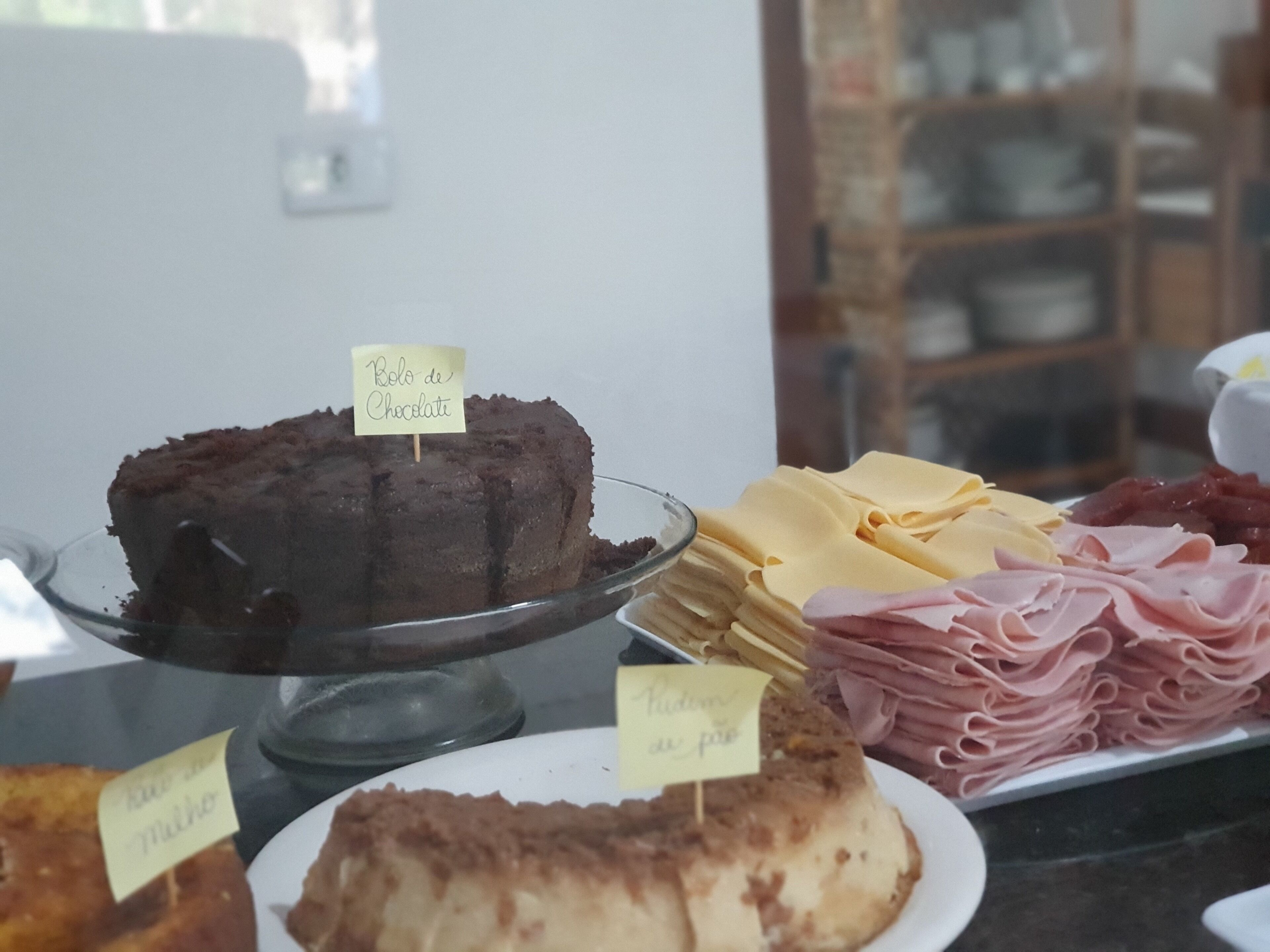 A dessert display with a chocolate cake and a vanilla cake, along with various cheeses and meats.