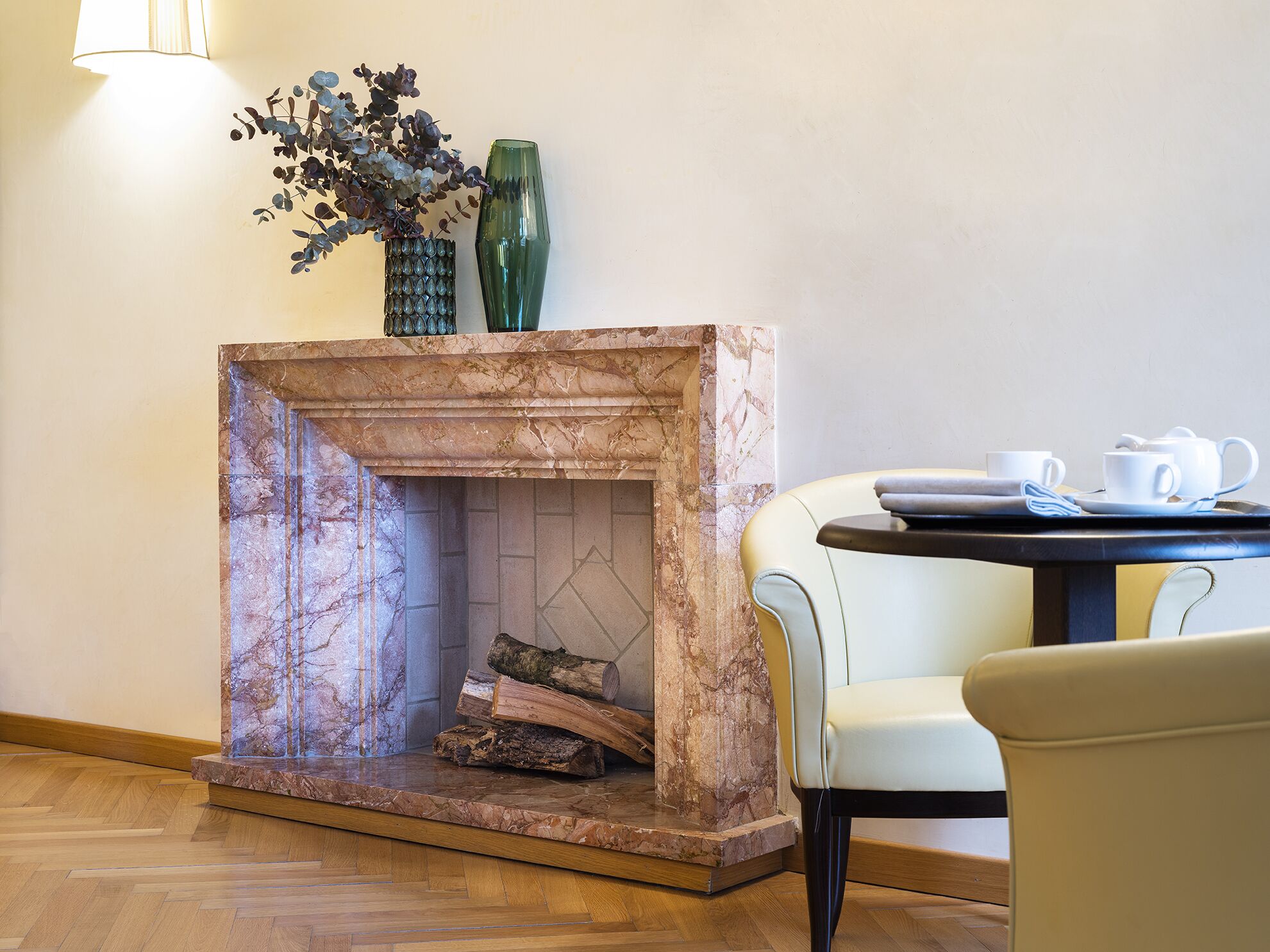 A marble fireplace with logs, a vase with flowers, and a table with cups and a tray.