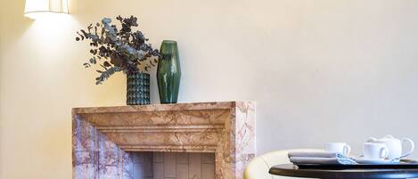 A marble fireplace with logs, a vase with flowers, and a table with cups and a tray.