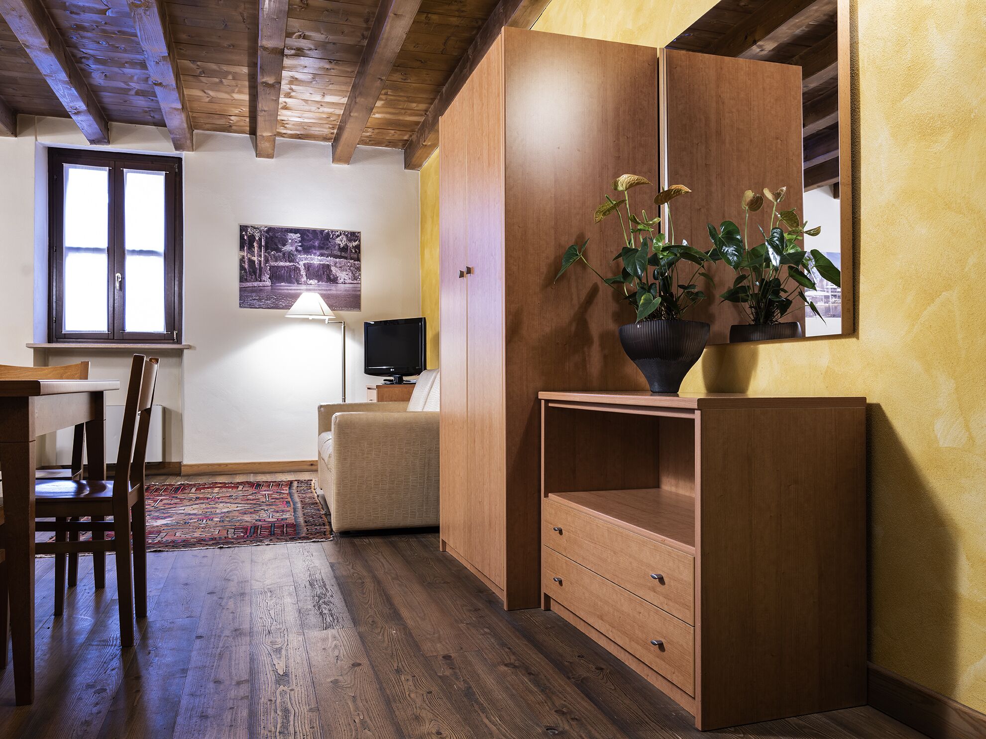 Una habitación acogedora con techo de madera, una mesa de comedor con sillas, un sofá, un televisor y una planta sobre un mueble de madera.