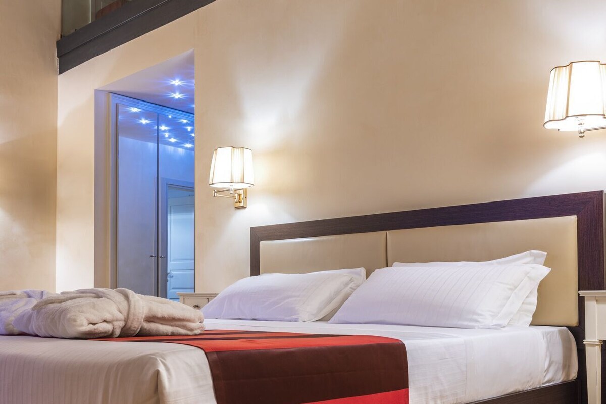 A hotel room with a bed, a nightstand, a lamp, and a ceiling with exposed beams.
