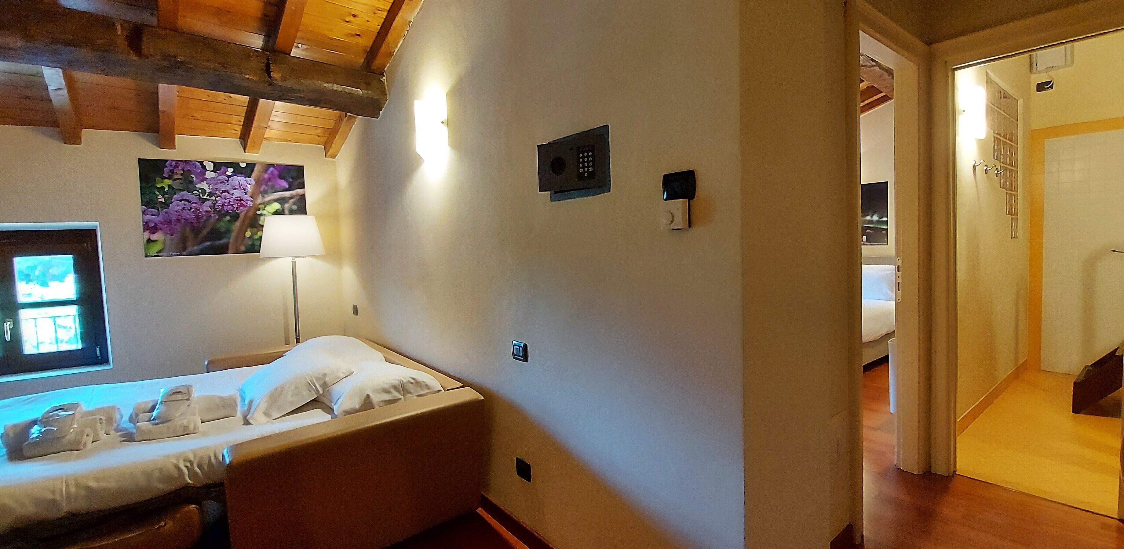 Une chambre d’hôtel avec un lit, un panneau de commande fixé au mur, un tableau représentant des fleurs et une fenêtre donnant sur un paysage.