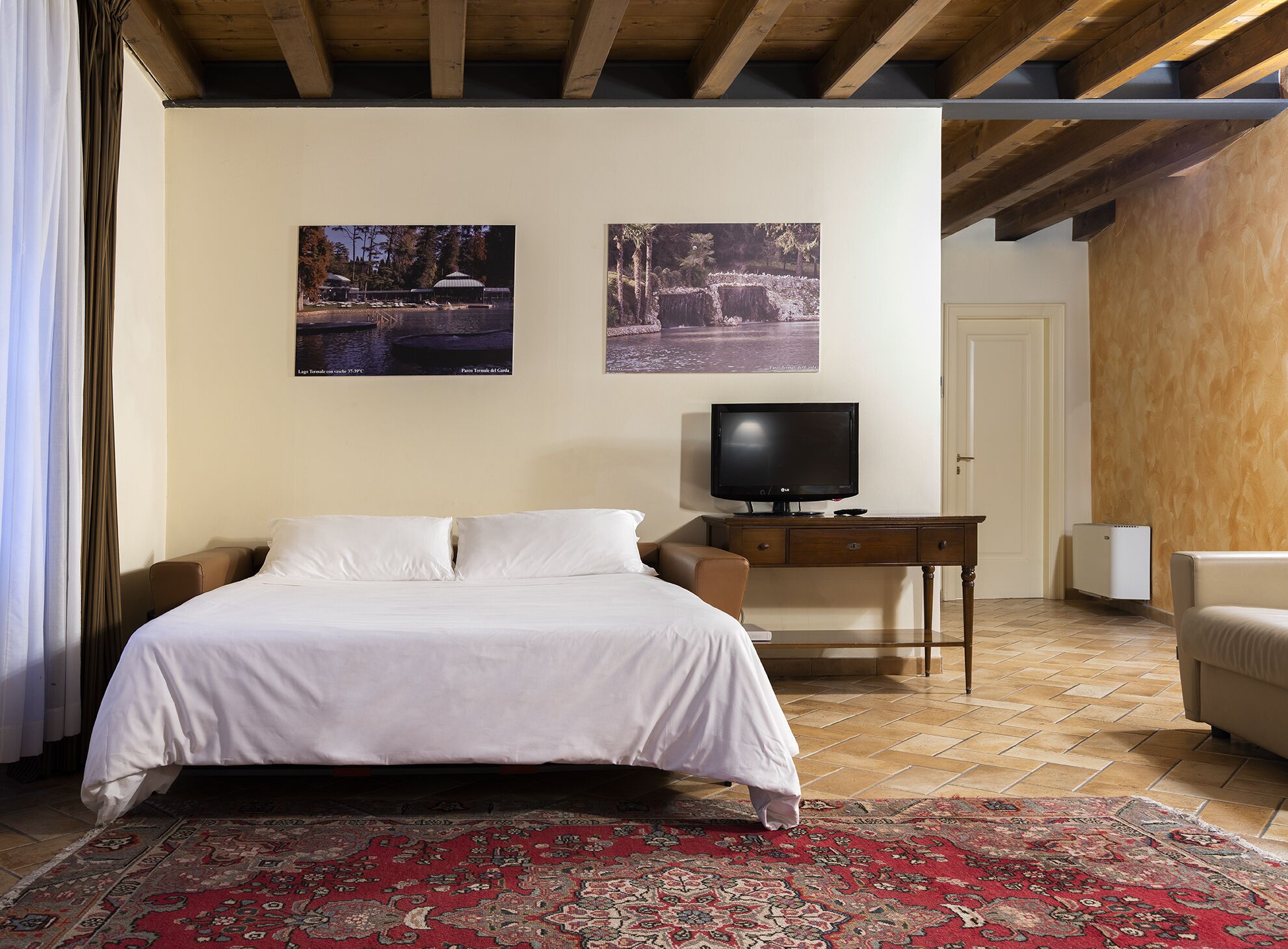 Una habitación de hotel con cama, televisión, escritorio y dos cuadros en la pared.