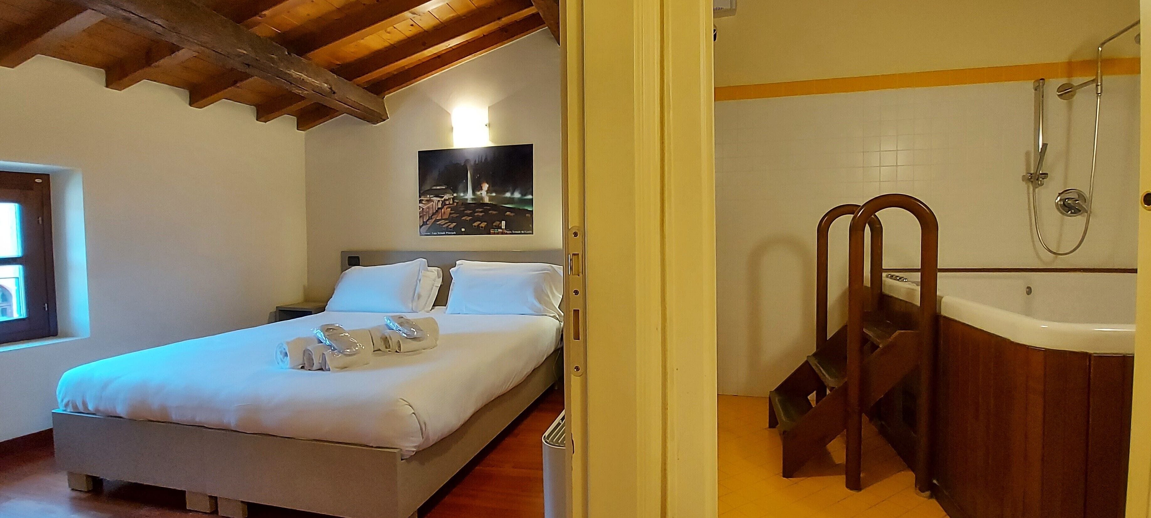 A bedroom with a bed, a nightstand, a poster on the wall, and a bathroom with a bathtub and shower.