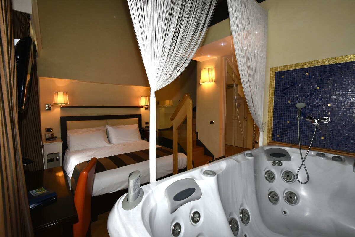 A hotel room with a bed, a desk, a chair, a bathroom with a bathtub, and a staircase.