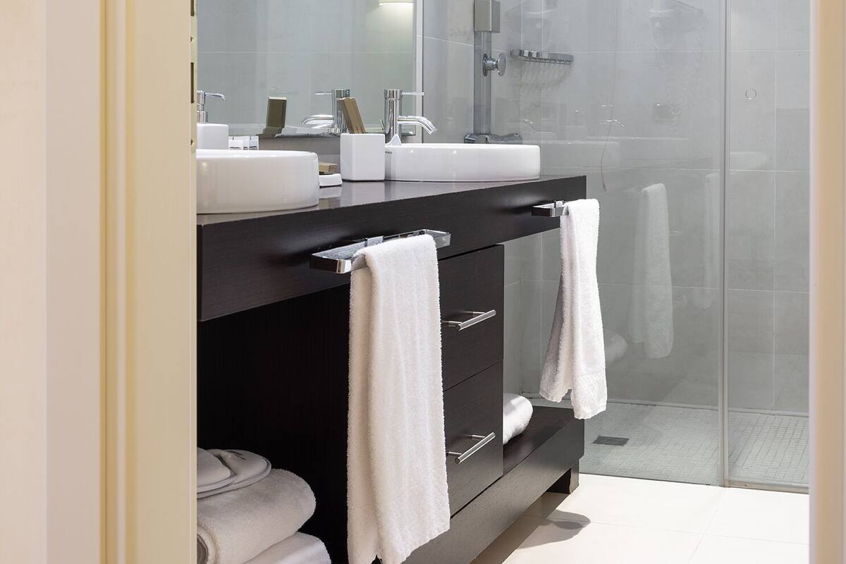 Un baño moderno con ducha de vidrio, tocador negro con espejo y dos toallas blancas.