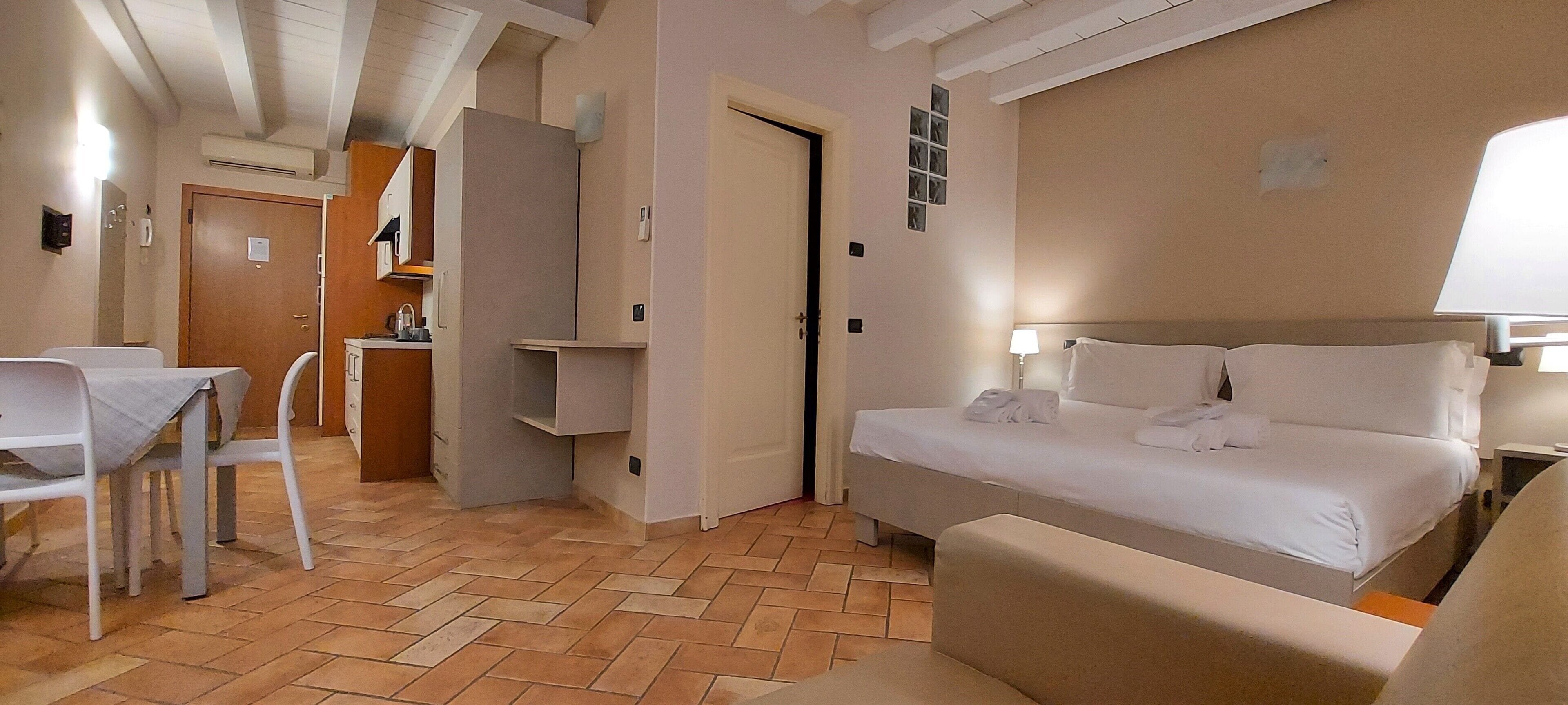 Habitación de hotel con cama, escritorio y silla. Hay una kitchenette en la esquina.