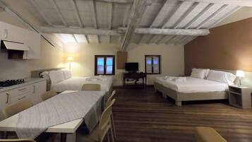 A hotel room with two beds, a desk, a TV, and a dining table.