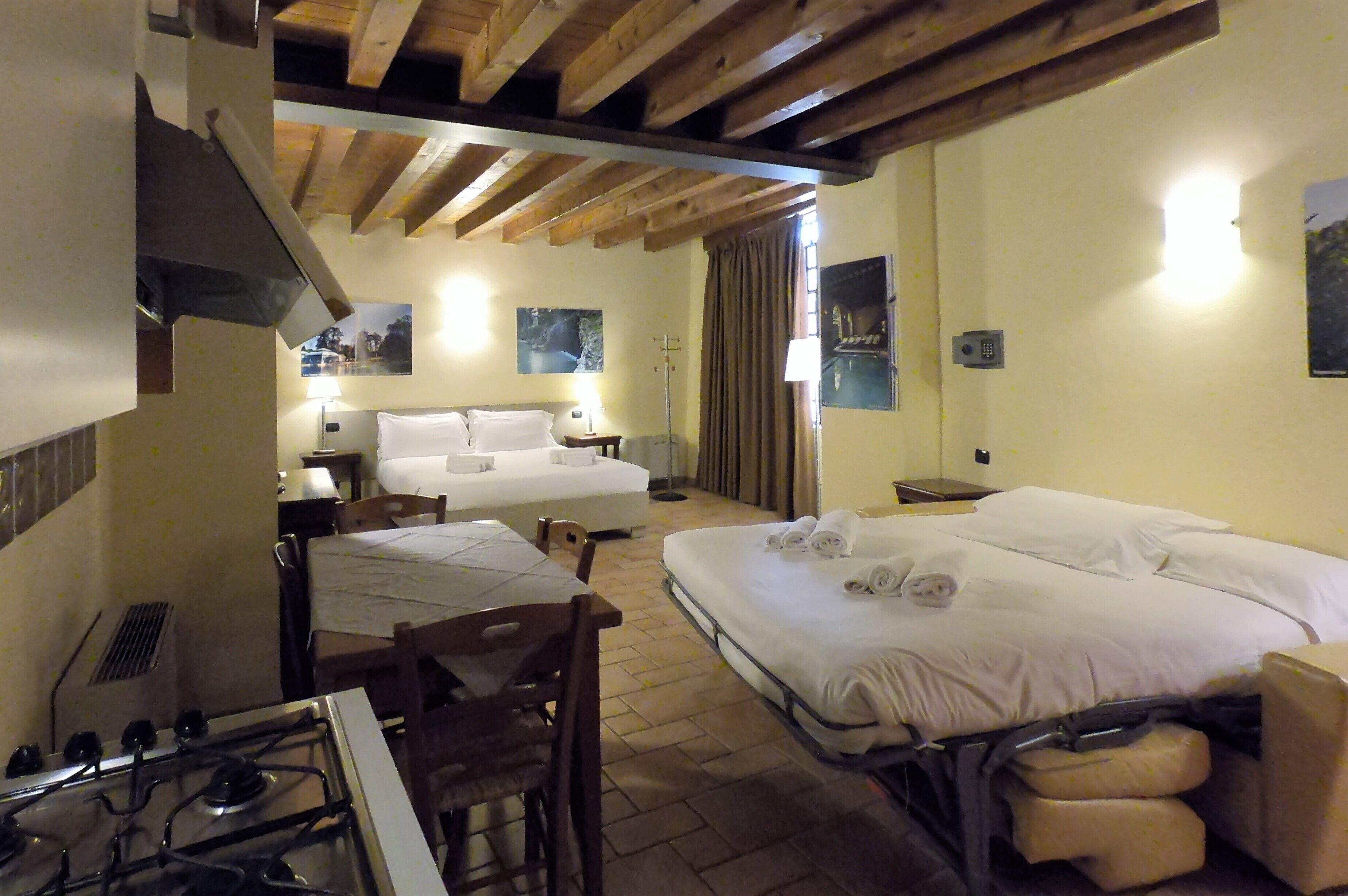 Quarto de hotel com cama, escrivaninha, cadeira, fogão e janela com cortinas.
