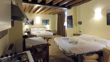 Quarto de hotel com cama, escrivaninha, cadeira, fogão e janela com cortinas.