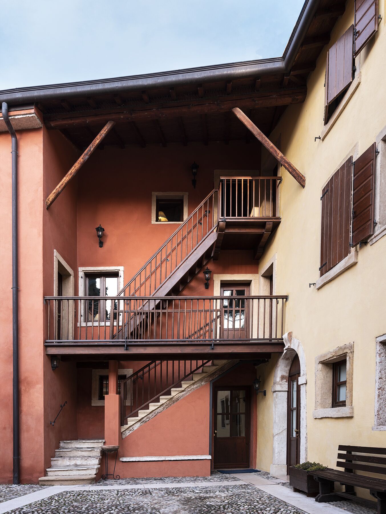 A building with a staircase leading to a balcony, a door, and a bench outside.