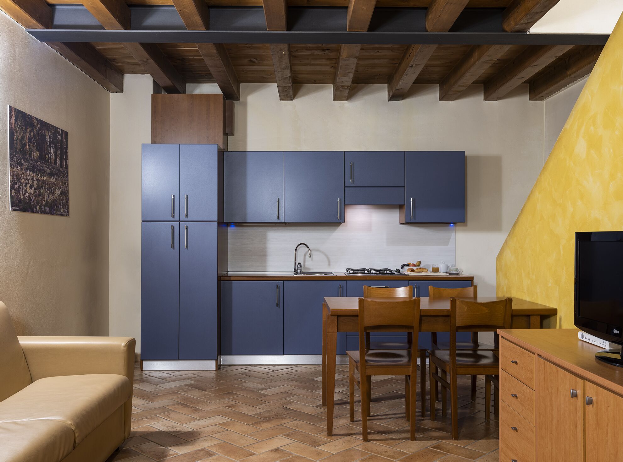Una cocina pequeña con armarios azules, una mesa de madera y sillas.