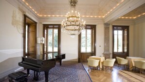 Une vaste pièce agrémentée d’un magnifique piano à queue, d’un lustre et d’un tapis à motifs.