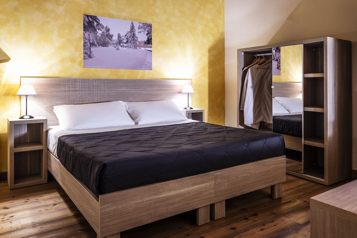 Una cama bien hecha con cabecera de madera, dos mesitas de noche y un armario con espejo.