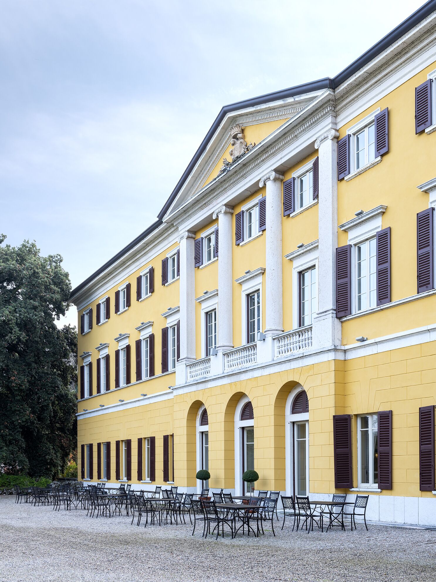 Un edificio giallo con colonne e finestre ad arco, area esterna con tavoli e sedie.