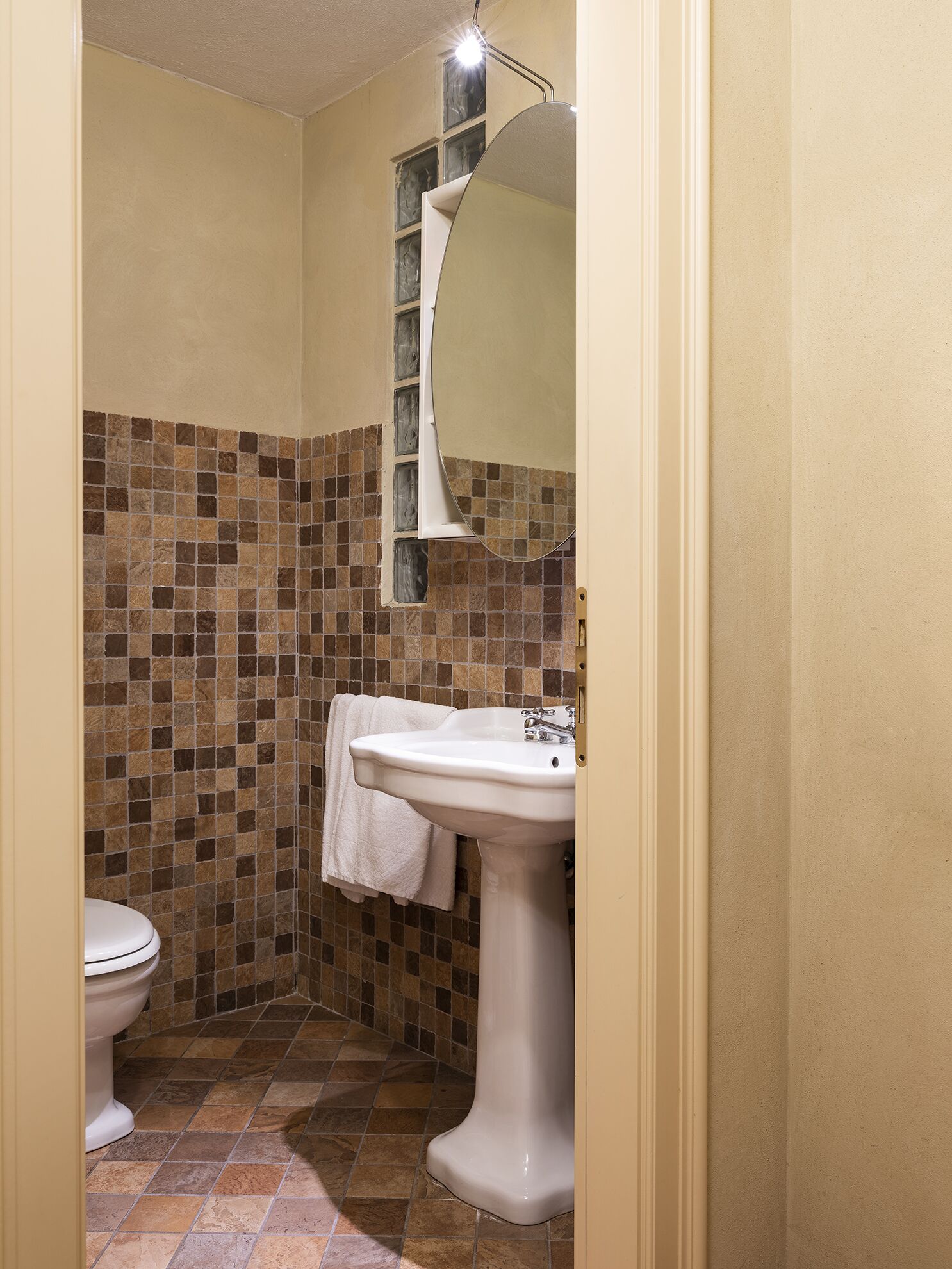 Et badeværelse med toilet, vask med spejl og fliservæg.