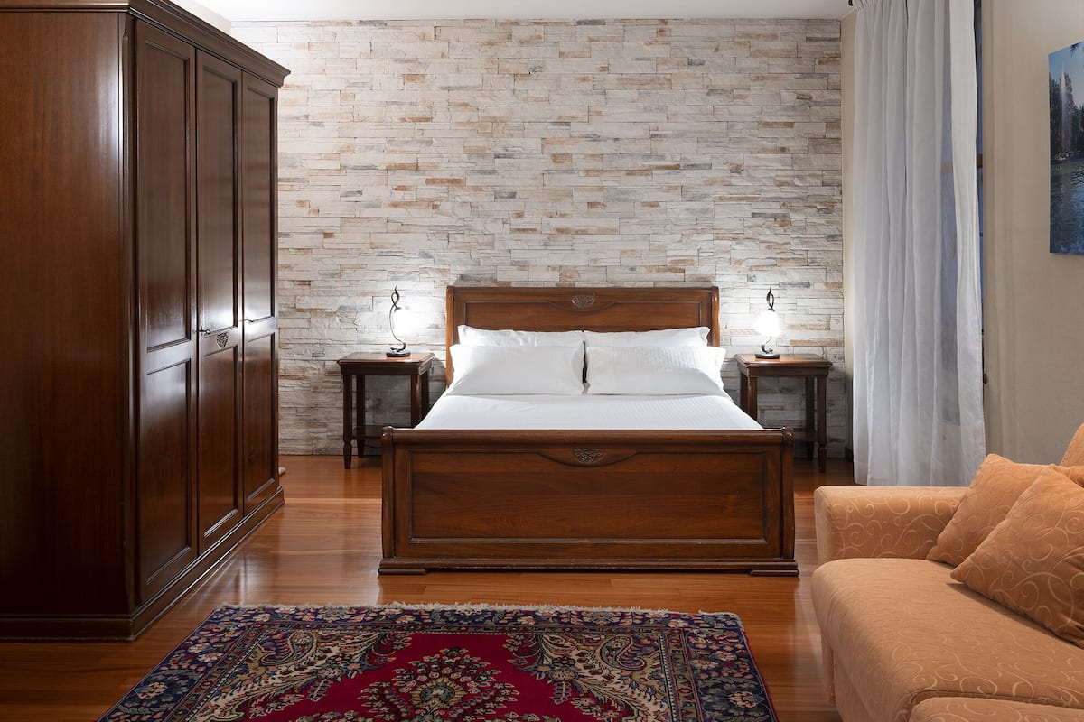 Un dormitorio con cama de madera, una mesita de noche, un armario, un tapete estampado y un sofá.