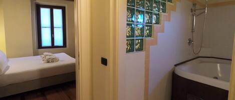 A room with a bed, a window, a shower, and a bathtub.