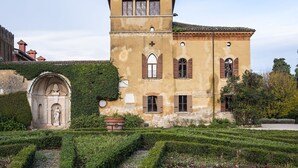 Un bâtiment historique doté d’une tour, d’une entrée en arc de cercle et d’un jardin agrémenté de haies.