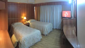 A hotel room with two beds, a desk, a television, and a lamp.