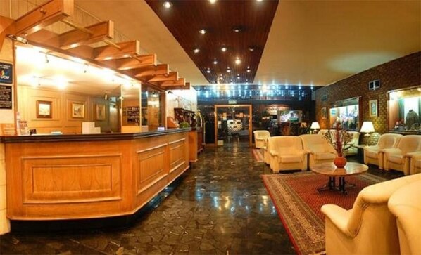Un vestíbulo de hotel con un mostrador de recepción de madera, una escalera y una zona de estar con sofás y una mesa de centro.