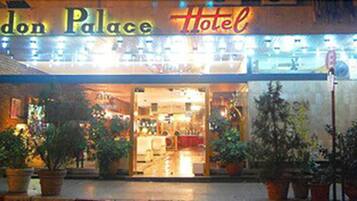 The exterior of the London Palace Hotel with a brightly lit entrance and potted plants in front.