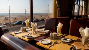 A restaurant table set with plates, cutlery, and napkins, with a view of the beach and cars in the background.
