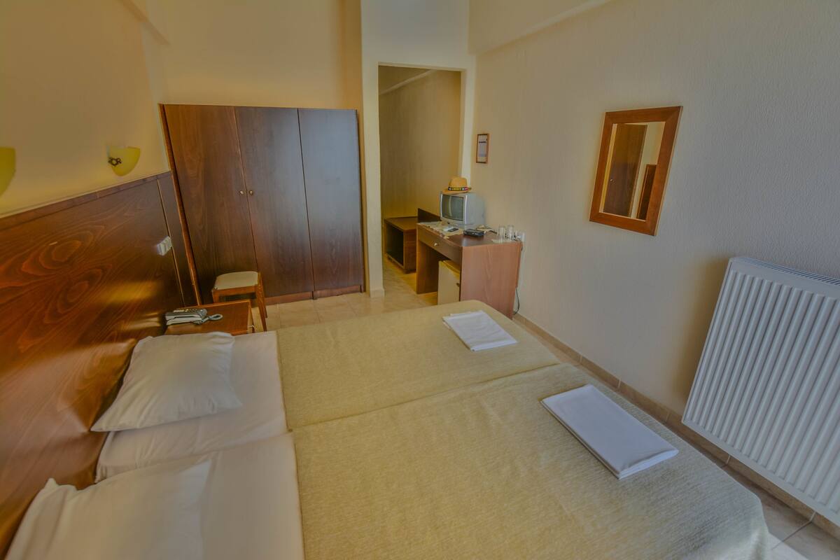 Habitación de hotel con dos camas, un escritorio, una silla, un televisor y un armario.