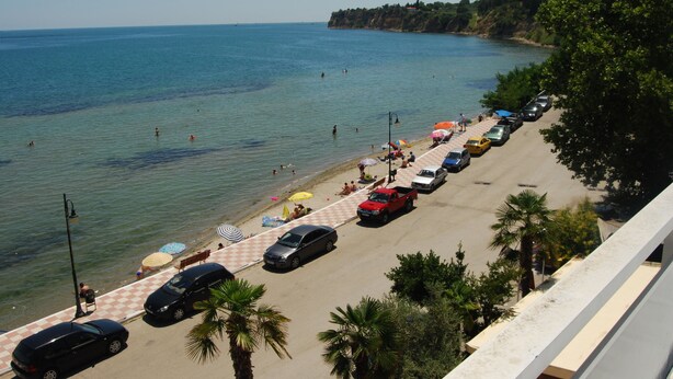Una playa con coches aparcados, sombrillas, cielo despejado y mar tranquilo.
