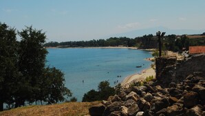 Vista costera con playa, terreno rocoso y una cadena montañosa distante.