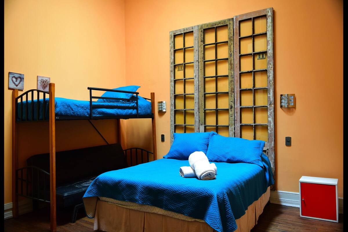 Habitación con literas, una colcha azul, una mesita de noche pequeña y un armario rojo.