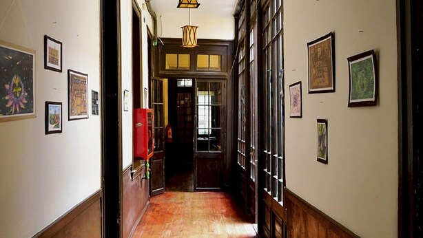 A hallway with wooden floors, framed artwork on the walls, and hanging lantern-style lights.