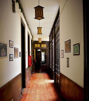 A hallway with wooden floors, framed artwork on the walls, and hanging lantern-style lights. - Santiago Backpackers (Santiago)