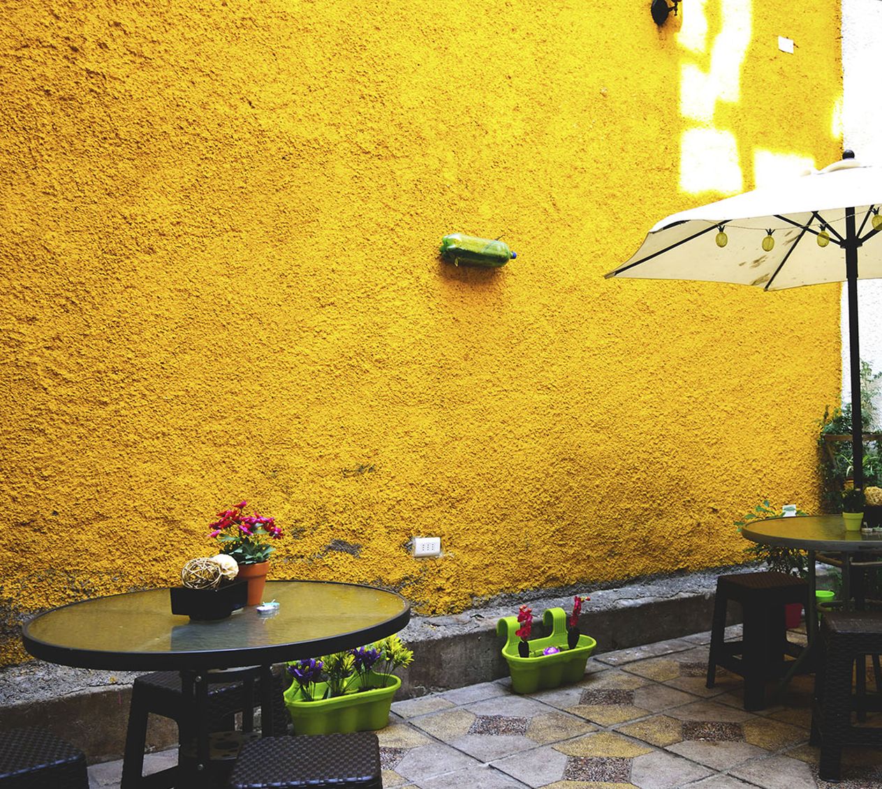 An outdoor patio with yellow textured walls, round tables, and potted plants.